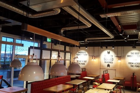 Smashburger, Dunfermline - low hanging white lamp shades, industrial exposed pipework in ceiling, red leather booth seating with wooden tables 
