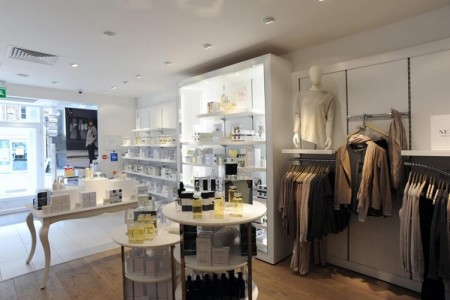 The White Company, Stamford - white display tables with fragrances, white cabinets with white looking products, clothes displays hanging on walls, half wooden floor and half white tiles