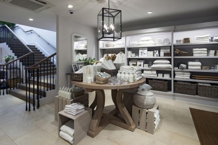 The White Company, Norwich - wooden table next to bottom of stairs, filled with soaps, diffusers, towels, all white