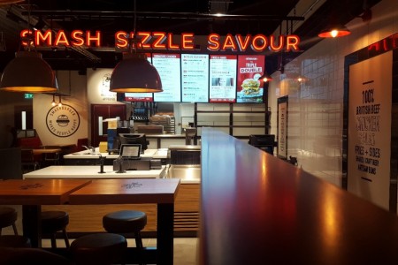 Smashburger, Dunfermline - dimmed lighting inside with white tiles on walls, oversized lamp shades, wooden tables and stools, POS with menus behind