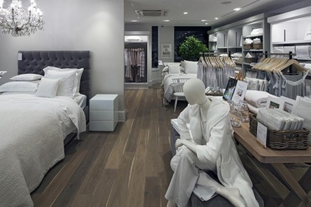 The White Company, Norwich - hardwood flooring, mannequin wearing white dressing gown, bespoke wooden table with white products on, white bed linen on bed