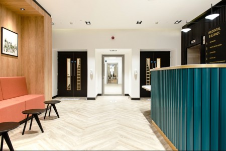 Prudential Buildings, Bristol - light wooden floor, seating area to the left with small tables, teale reception desk to the right, doors in front