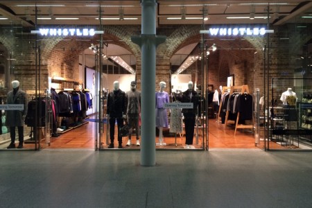 Whistles, St Pancras Station, London - large glass shopfront with wooden floor inside, mannequins and clothing displays visible, brick arches 