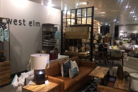 West Elm - sofa with side table and lamp, coffee table, shelving unit, West Elm logo on wall behind