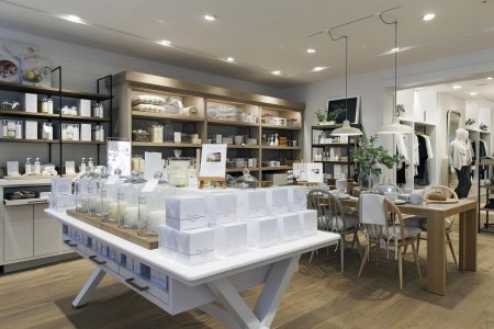 The White Company, Norwich - white table with white boxes of candles and white candles in jars, wooden table and chairs behind