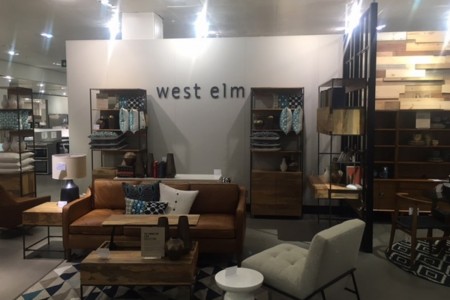 West Elm - sofa with side table and lamp, coffee table, grey chair, shelving unit, West Elm logo on wall behind