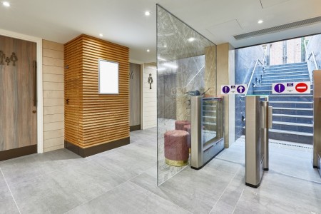 Princesshay Shopping Centre public toilets, Exeter - wooden panelling by entrance/exit with seating area and large plant, grey tiled floor
