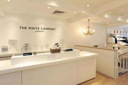 The White Company, Stamford - white desk with tills behind, black company logo on white wall behind