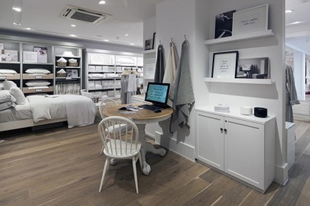 The White Company, Norwich - POS with computer on wooden table and two white chairs. White walls and cupboards around it