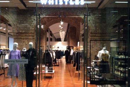 Whistles, St Pancras Station, London - large glass shopfront with wooden floor inside, mannequins and clothing displays visible, brick arches 