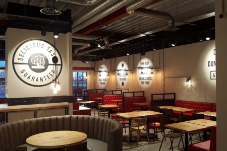Smashburger, Dunfermline - circular grey booth seating with wooden tables and chairs around, also red leather booth seating, industrial exposed ceiling