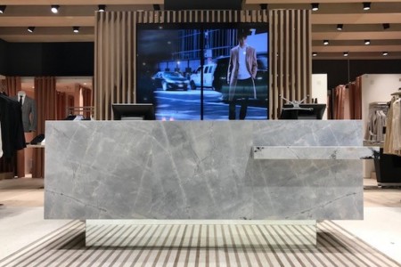 Reiss, Canary Wharf - large screen with advertising behind stone-looking till area and wooden panelling surrounding