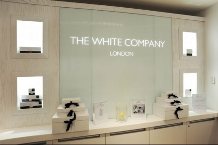 The White Company, Stamford - white wall with white logo on a glass background, white boxes with black ribbons 