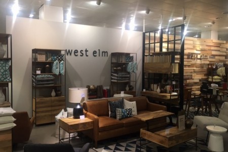 West Elm - sofa with side table and lamp, coffee table, shelving unit, West Elm logo on wall behind
