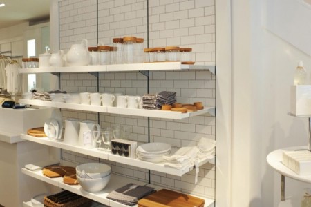 The White Company, Stamford - white tiled wall with white shelves, white and wooden kitchen items such as bowls, jugs, jars