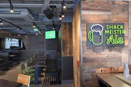 Shake Shack, Leicester Square - natural wood clad walls with neon green and white sign, bench seating 